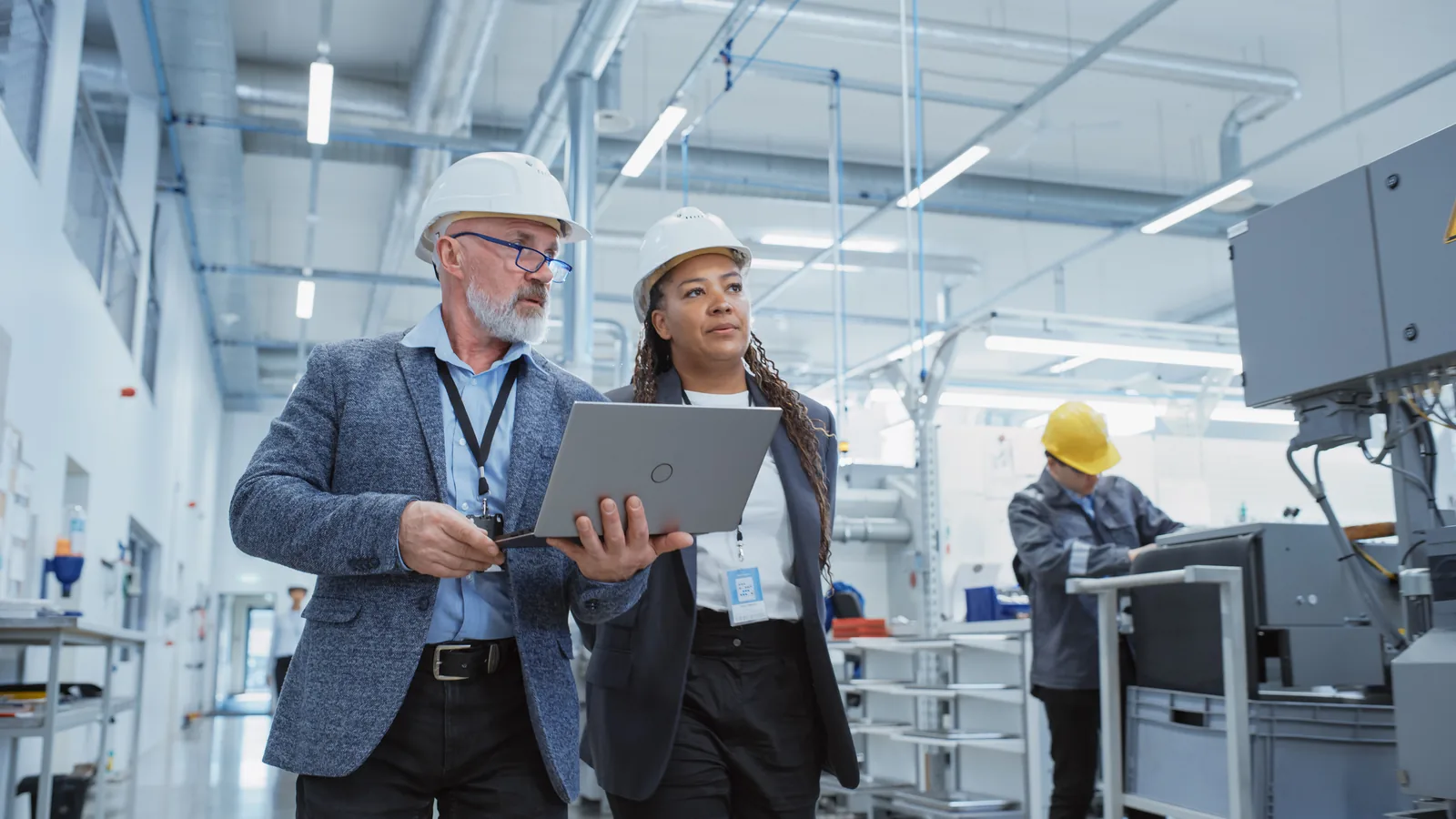 Two colleagues in hard hats reviewing information on a laptop in a factory